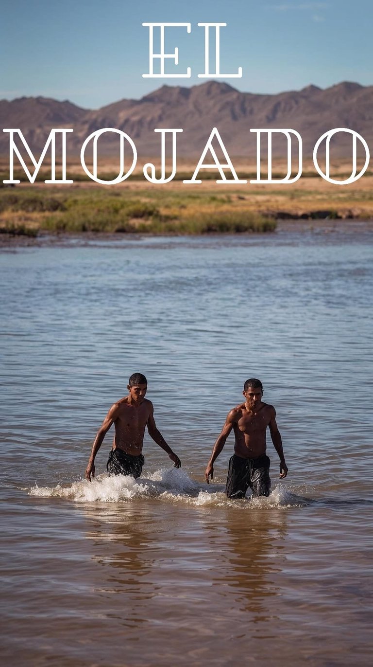 Two men wading in a river with desert mountains and text El Mojado overlaid